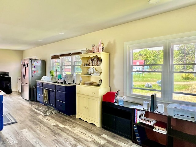 kitchen with stainless steel fridge, sink, blue cabinets, and light wood-type flooring