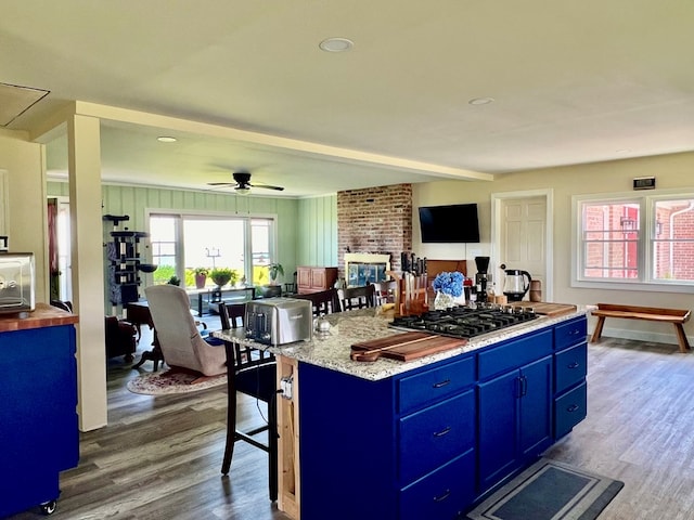 kitchen featuring dark wood-type flooring, black gas stovetop, blue cabinets, ceiling fan, and a kitchen island