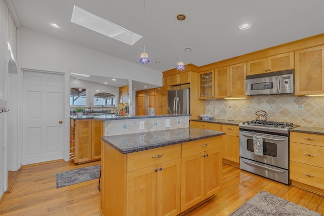 kitchen with stainless steel appliances, glass insert cabinets, a kitchen island, dark stone countertops, and vaulted ceiling with skylight