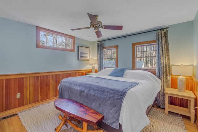 bedroom with light wood finished floors, a ceiling fan, wood walls, and wainscoting