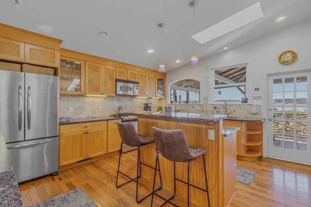 kitchen with dark stone counters, a kitchen island, glass insert cabinets, a breakfast bar, and stainless steel appliances