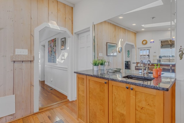 kitchen with light wood-type flooring, a sink, wooden walls, and dark stone countertops