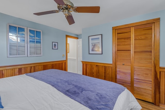 bedroom featuring wooden walls, a ceiling fan, a closet, and wainscoting