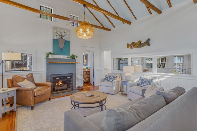 living room with lofted ceiling with beams, a brick fireplace, wainscoting, wood finished floors, and a chandelier