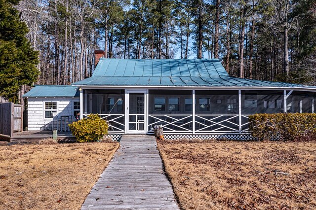 view of front facade featuring a sunroom, metal roof, a chimney, and a standing seam roof