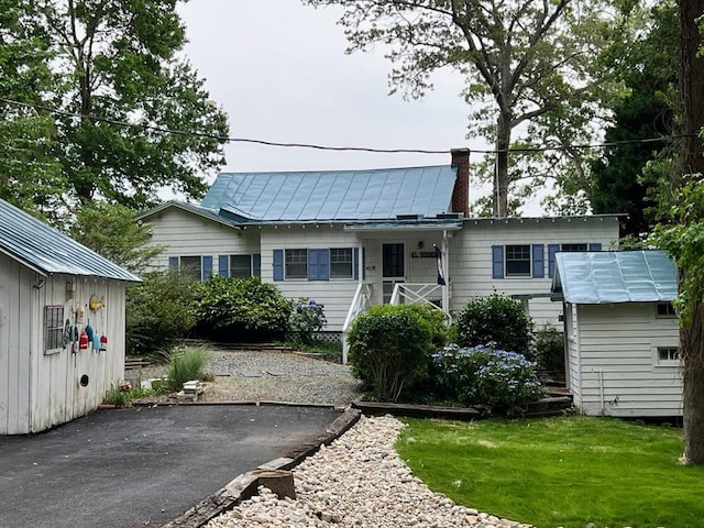 view of front of property with driveway, a chimney, metal roof, a standing seam roof, and a front yard