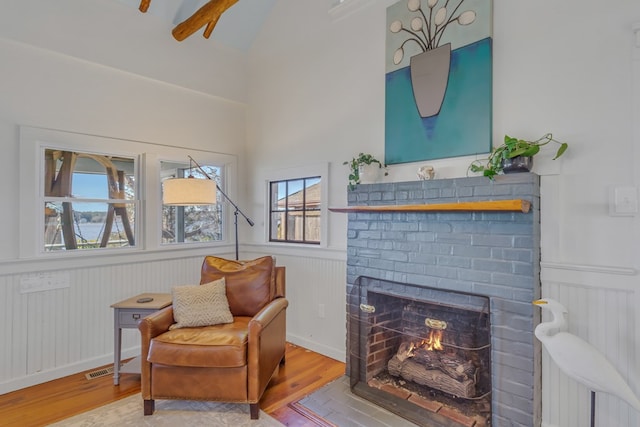 living area featuring wainscoting, a fireplace, visible vents, and wood finished floors