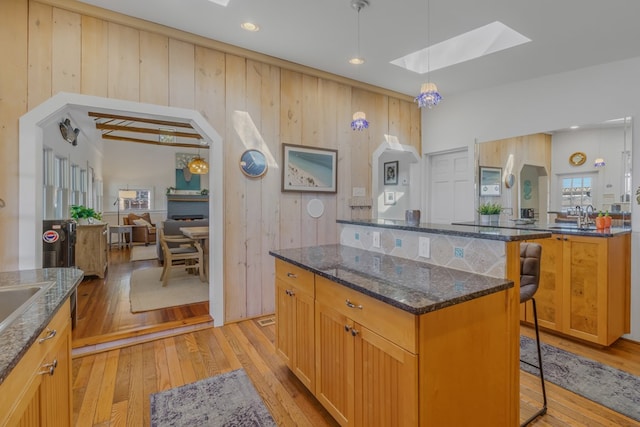 kitchen with a skylight, a center island, light wood finished floors, a breakfast bar area, and dark stone countertops