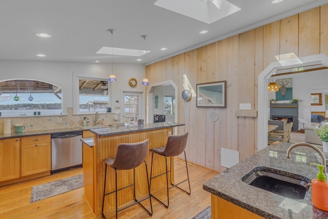 kitchen with a skylight, a kitchen island with sink, a sink, and stainless steel dishwasher