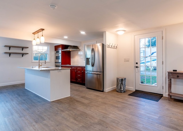 kitchen featuring sink, wall chimney exhaust hood, decorative light fixtures, appliances with stainless steel finishes, and hardwood / wood-style flooring