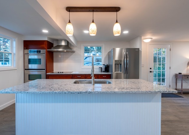 kitchen with appliances with stainless steel finishes, tasteful backsplash, wall chimney exhaust hood, sink, and decorative light fixtures