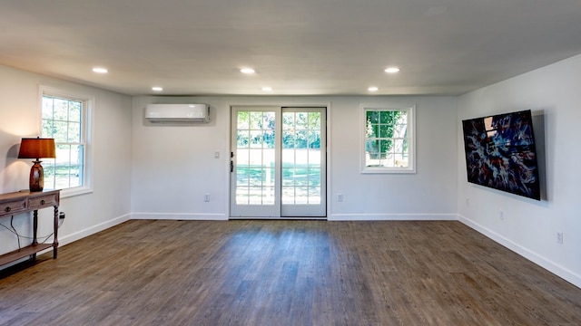 unfurnished room featuring dark hardwood / wood-style floors, a wall unit AC, and a healthy amount of sunlight