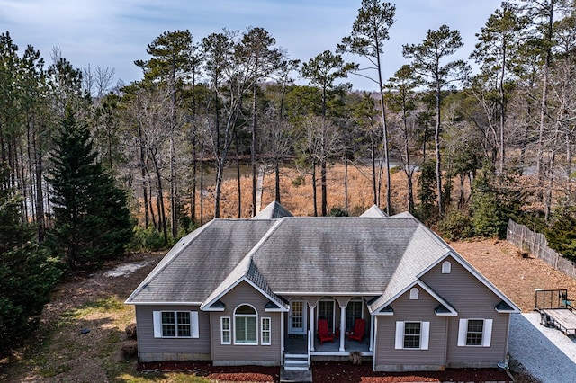 view of front facade with a porch, roof with shingles, fence, and a forest view