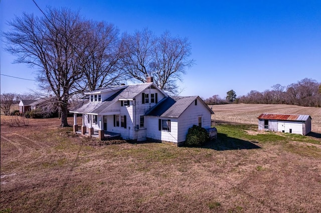 view of side of property with an outbuilding, a porch, a rural view, and a lawn