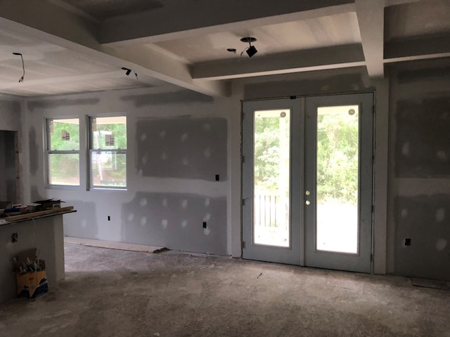 unfurnished living room featuring beam ceiling, a wealth of natural light, and french doors