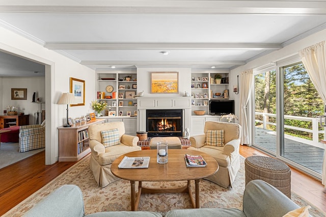 living room with a lit fireplace, crown molding, built in features, beamed ceiling, and light wood finished floors
