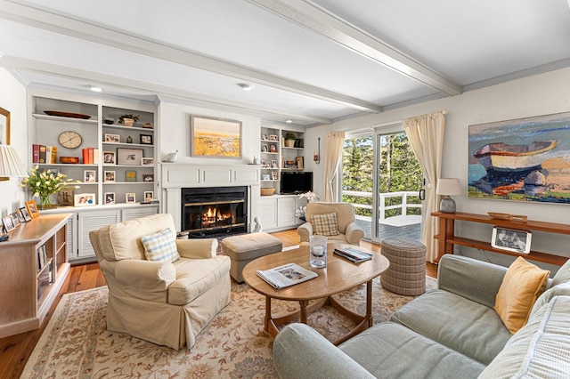 living room featuring beamed ceiling, a glass covered fireplace, and wood finished floors