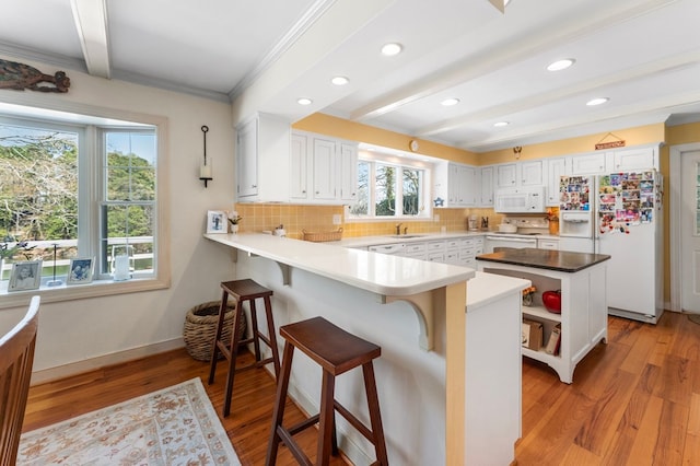 kitchen featuring backsplash, white cabinetry, a peninsula, white appliances, and light wood-style flooring
