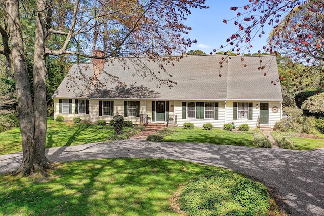 ranch-style house featuring roof with shingles, a chimney, and a front yard
