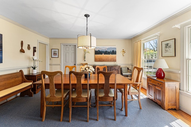 dining room featuring ornamental molding, light wood-style flooring, and a wainscoted wall