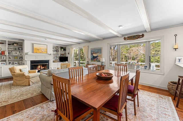 dining room featuring baseboards, a glass covered fireplace, wood finished floors, and beam ceiling
