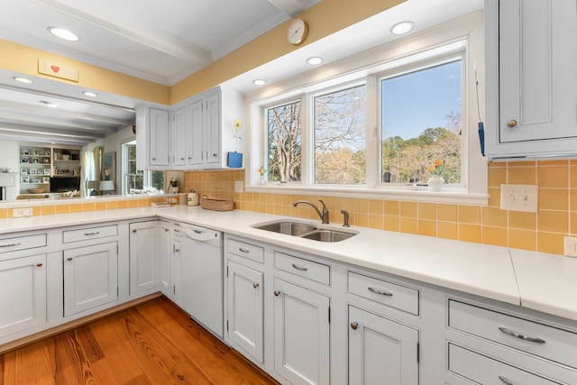 kitchen with light wood-style floors, white dishwasher, light countertops, tasteful backsplash, and a sink