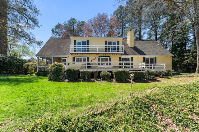 rear view of property with a lawn, a chimney, a sunroom, and a balcony