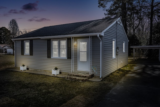 view of front of home with a yard, a carport, and a shingled roof