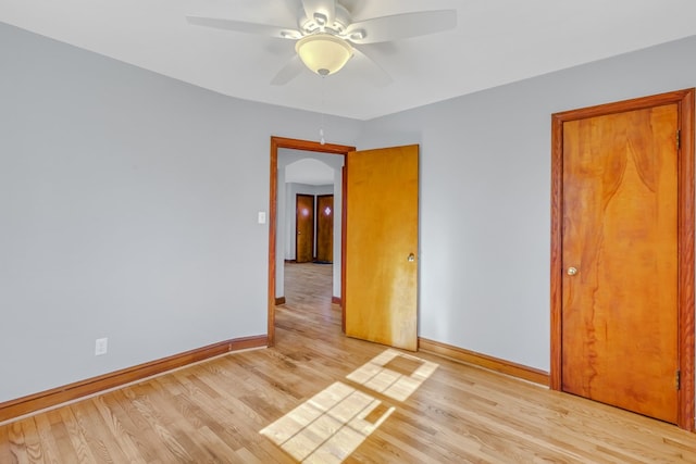 unfurnished room featuring baseboards, arched walkways, light wood-style floors, and ceiling fan