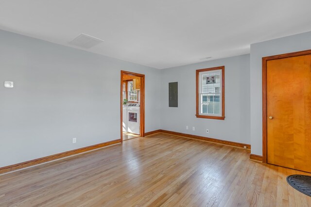 empty room featuring electric panel, visible vents, light wood-type flooring, and baseboards