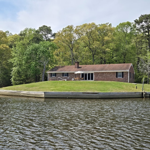 rear view of house with a chimney, a forest view, a yard, and a water view