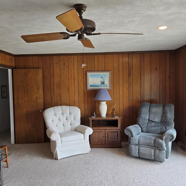 living area with wooden walls, a textured ceiling, carpet flooring, and ceiling fan