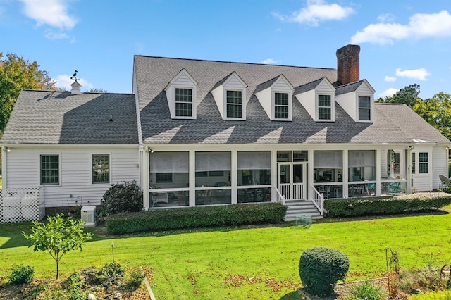 back of property with a sunroom, roof with shingles, a yard, and a chimney