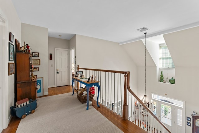 hallway featuring visible vents, vaulted ceiling, an upstairs landing, and wood finished floors