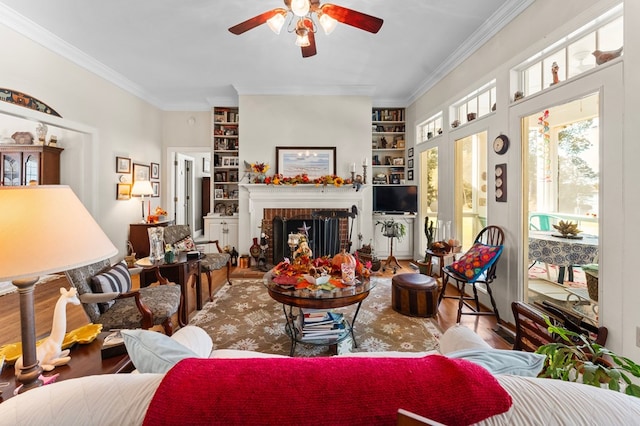 living area featuring a brick fireplace, built in shelves, ornamental molding, and wood finished floors