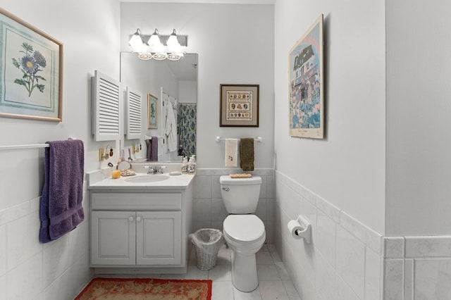 bathroom with tile patterned flooring, toilet, a wainscoted wall, vanity, and tile walls