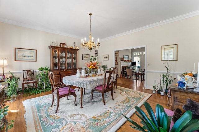 dining space with a notable chandelier, a fireplace, ornamental molding, and wood finished floors