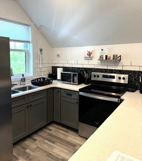 kitchen featuring sink, hardwood / wood-style flooring, appliances with stainless steel finishes, decorative backsplash, and vaulted ceiling