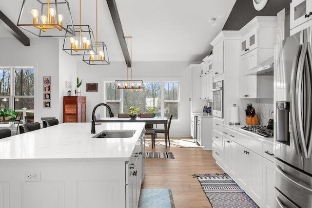 kitchen with a chandelier, stainless steel appliances, a sink, an island with sink, and beam ceiling