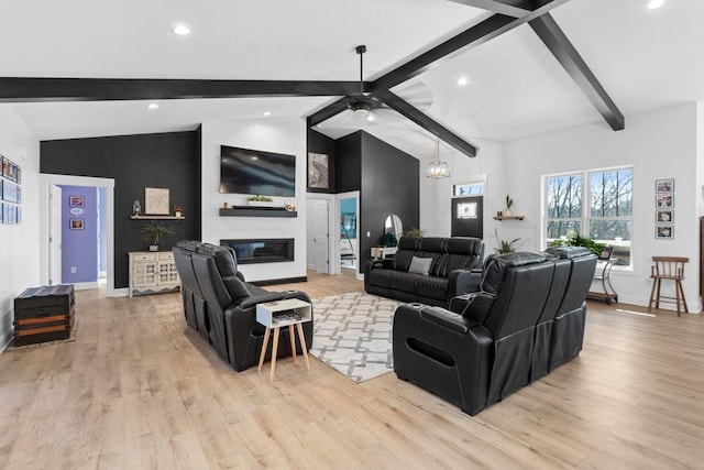 living room featuring ceiling fan, vaulted ceiling with beams, a fireplace, and light hardwood / wood-style floors