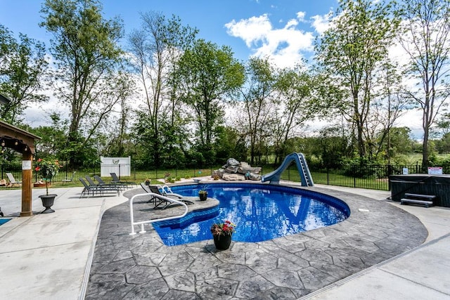 view of swimming pool with a water slide, a patio, fence, and view of scattered trees