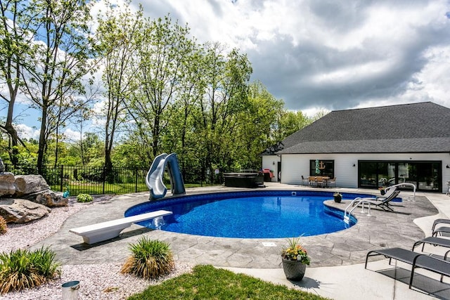 view of pool with a hot tub, fence, a diving board, a patio, and a water slide