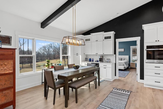 dining area featuring a chandelier, light wood finished floors, beam ceiling, baseboards, and high vaulted ceiling