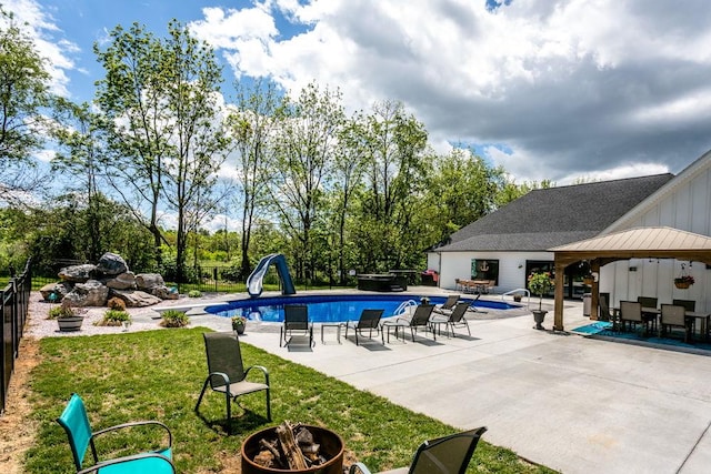 swimming pool featuring a water slide, a patio area, a fire pit, outdoor dining space, and view of wooded area