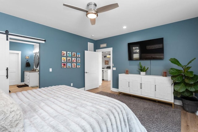 bedroom with a barn door, ceiling fan, and light hardwood / wood-style flooring