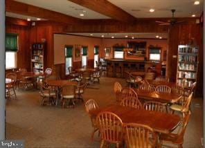 dining room with beamed ceiling, ceiling fan, and wood walls