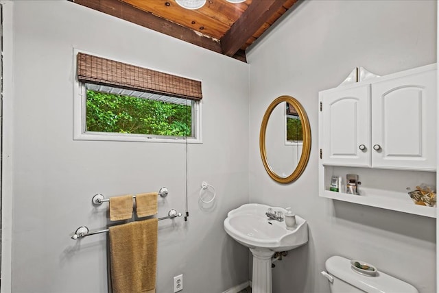 bathroom with beamed ceiling, toilet, and sink