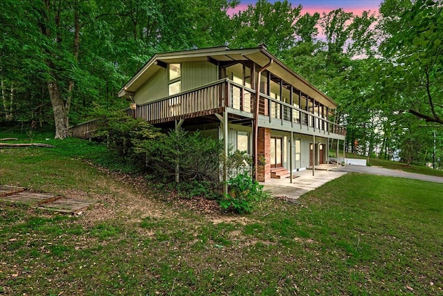 property exterior at dusk with a patio area, a yard, and a deck