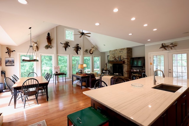 kitchen with light wood-type flooring, vaulted ceiling, ceiling fan, sink, and an island with sink