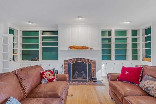 living room with a fireplace, light wood-type flooring, built in features, and crown molding